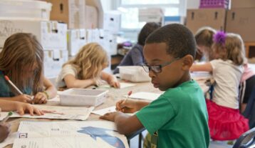 boy in green sweater writing on white paper